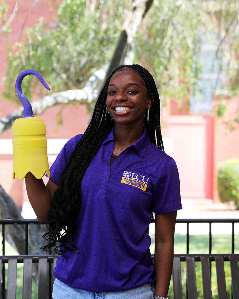 female student wearing a purple ECU polo and holding a 3D printed hook
