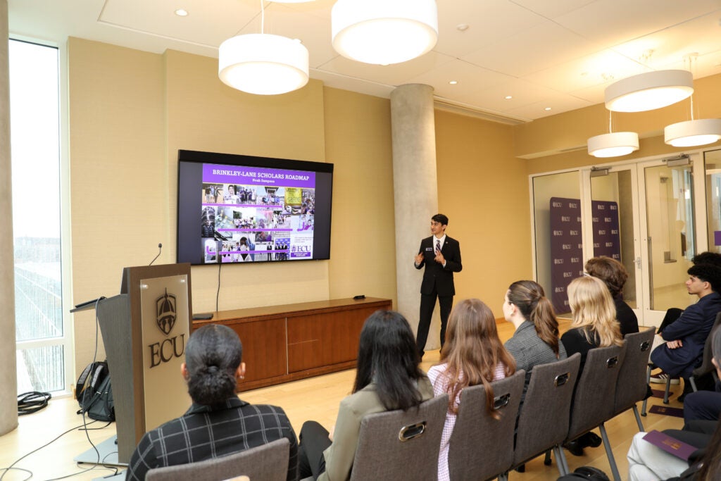 male student standing beside projector screen in front of audience