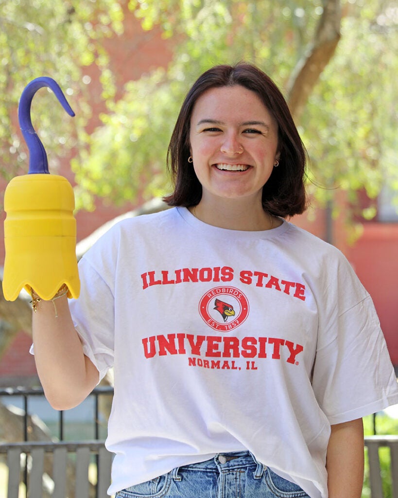 female student wearing a white shirt with Illinois State University on it and holding a 3D printed hook