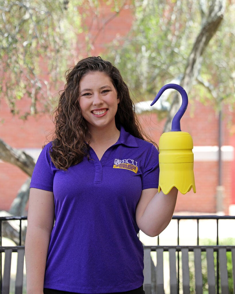 female student wearing a purple ECU polo and holding a 3D printed hook