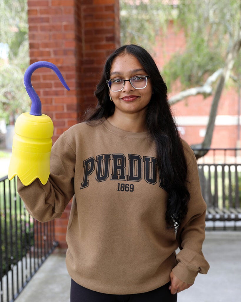 female student wearing brown sweatshirt with Purdue written on it and holding a 3D printed hook