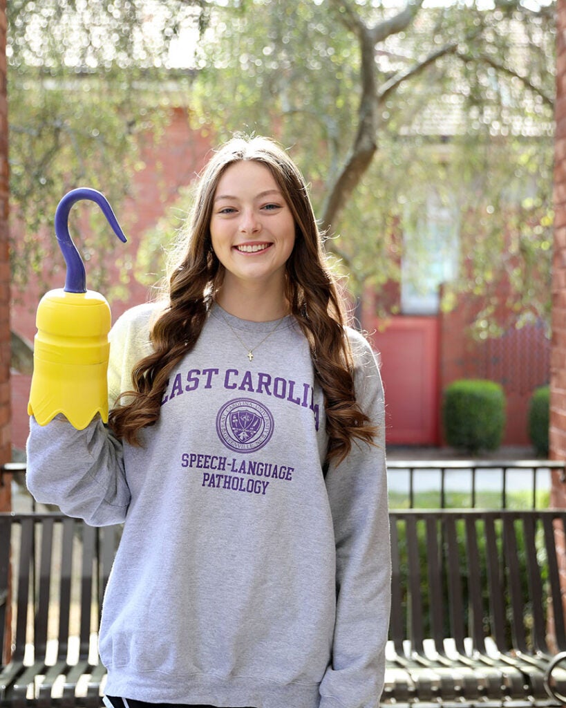 female student wearing gray sweatshirt with East Carolina speech-language pathology on it and holding a 3D printed hook