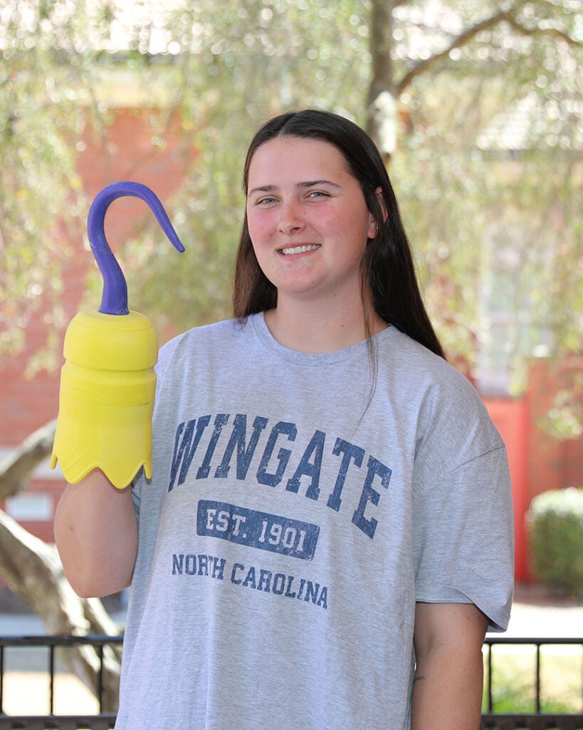 Female student wearing a gray t-shirt with the words Wingate Est. 1901 North Carolina and holding a 3D printed hook