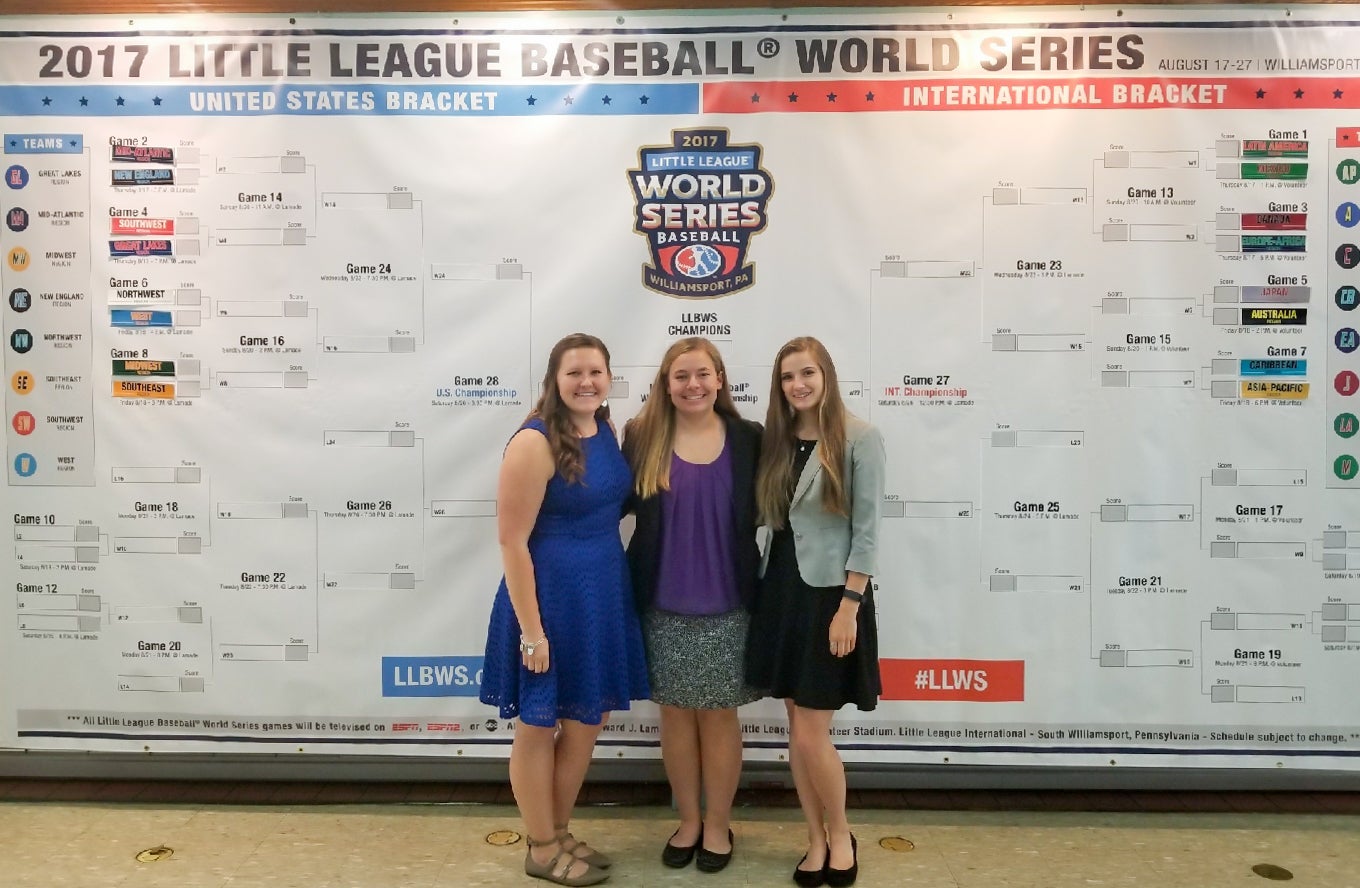 Ashely Weingartz, middle, stands with two other Little League World Series interns in front of the LLWS bracket during the Little League Luncheon. 