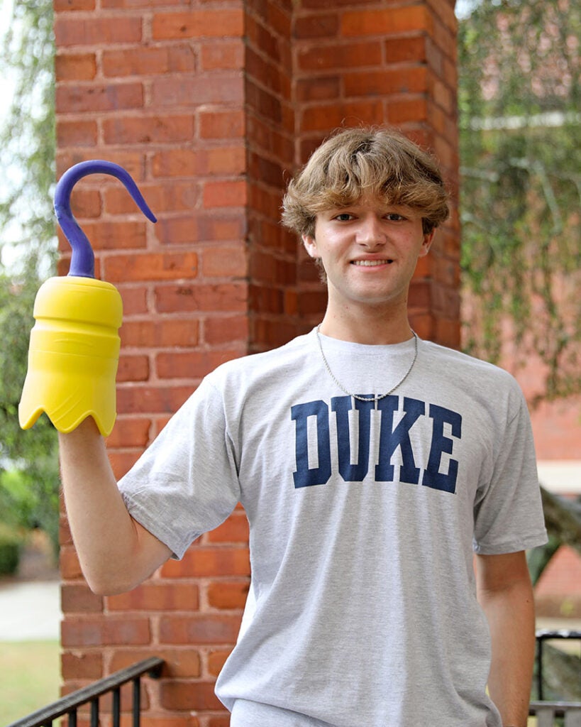 male student wearing a gray Duke shirt and holding a 3D printed hook